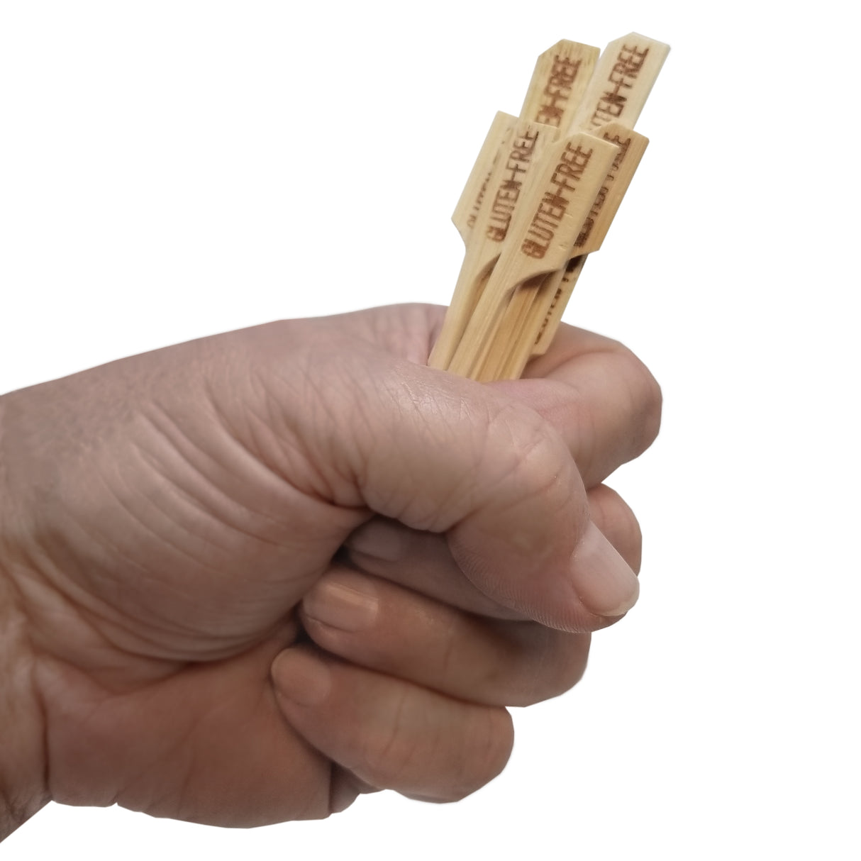 A hand is holding three bamboo meat marker picks with the words GLUTEN FREE engraved on each stick, isolated on a white background.