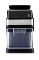 A front-facing view of a Waring countertop ice crusher machine. It features a sleek, stainless steel and black design with a transparent plastic container at the bottom to collect crushed ice. The on/off switch is visible near the top right corner.