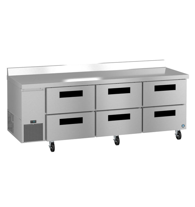 A Hoshizaki stainless steel worktop refrigerator with six pull-out drawers, black handles, and four caster wheels. It features a vented cooling section on the left and a raised backsplash along the back edge.