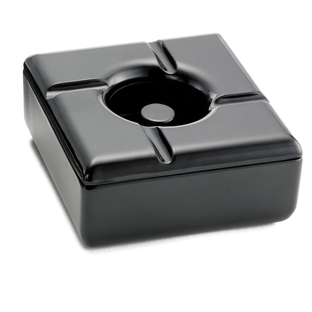A square black ceramic ashtray with rounded edges and four grooves for holding cigarettes, photographed on a white background. This windproof ashtray features a glossy surface that reflects light, and its recessed center is designed to catch ashes.