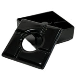 A black, square windproof ashtray with a removable lid. The lid features a central round opening and four notches for holding cigarettes. The deep melamine ashtray beneath is dishwasher safe and designed to catch ashes and butts.