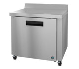 This ENERGY STAR stainless steel worktop refrigerator features a solid door with a black handle, small backguard, and four caster wheels. Its sleek, industrial design is accented by a round logo on the lower right corner.