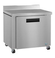 The Hoshizaki Steelheart worktop refrigerator features a single door, black handle, flat top, and small wheels for mobility. Its smooth, brushed stainless finish and ENERGY STAR rating ensure efficiency and style, with a blue logo at the bottom right corner.