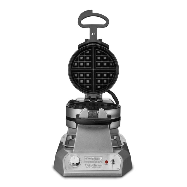 A silver and black double Belgian waffle maker with the lid open reveals a round, four-section waffle plate. The control panel below features a dial, indicator light, and Waring brand label. This commercial waffle maker sits on a white background.