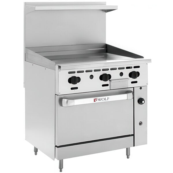 A stainless steel commercial restaurant range with a thermostatic griddle on top, six black control knobs, a large oven door labeled “Wolf,” and a backsplash with a small shelf above. The range stands on four adjustable legs.