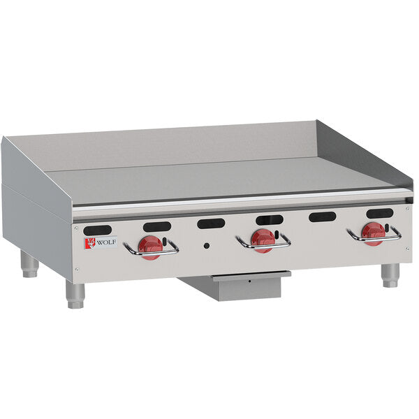 A heavy duty gas griddle, the Wolf AGM36_NAT is a stainless steel commercial countertop griddle with three red control knobs, a flat cooking surface, raised edges, sturdy metal legs, ventilation slots in front, and the Wolf logo on the left.