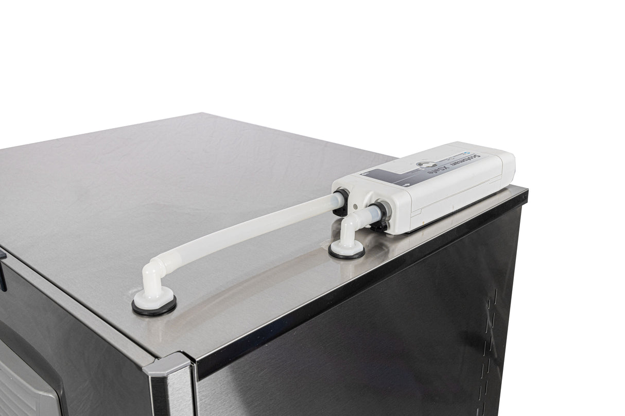 A white XSafe Sanitation System water filtration device with two connected hoses is mounted on top of a Scotsman modular cube ice machine against a plain white background. One hose enters the appliance, while the other connects to the filter unit.
