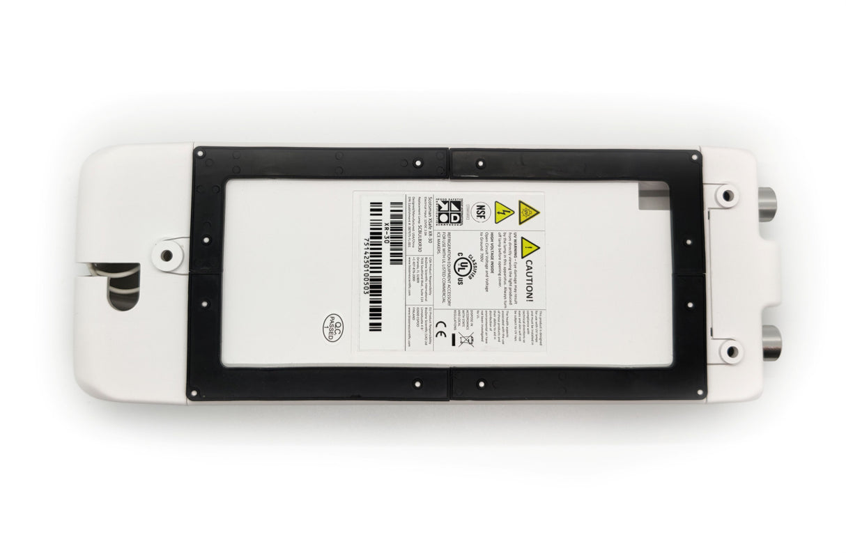 A rectangular white electronic device with a black frame surrounds a central label printed with barcodes, warning symbols, certifications, and technical information. Ideal for Scotsman modular cube ice machines or XSafe Sanitation System, it features rounded edges and metal ports on one side.