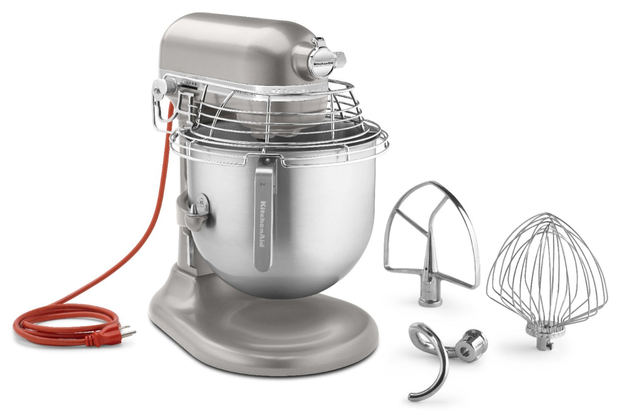 A silver KitchenAid Commercial Stand Mixer with an 8 quart metal mixing bowl and wire safety guard is shown. Beside it are three attachments: a flat beater, a dough hook, and a wire whisk. The mixer features a red power cord.