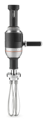 A heavy duty KitchenAid immersion blender with a silver and black body, side handle, and a metal whisk attachment at the bottom, shown upright on a plain white background.