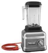 A silver KitchenAid Commercial Bar Blender with a transparent 60 oz. capacity pitcher, left-side handle, and measurement markings. The front features a dial, Start/Stop and Pulse buttons, and an orange power cord coiled beside it.