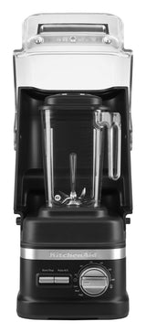 A black KitchenAid Commercial Blender with a clear 60 oz blending jar and lid sits on a counter. Its control panel features a silver dial, buttons, and display. A large clear sound enclosure covers the top and sides of this Enclosure Blender.