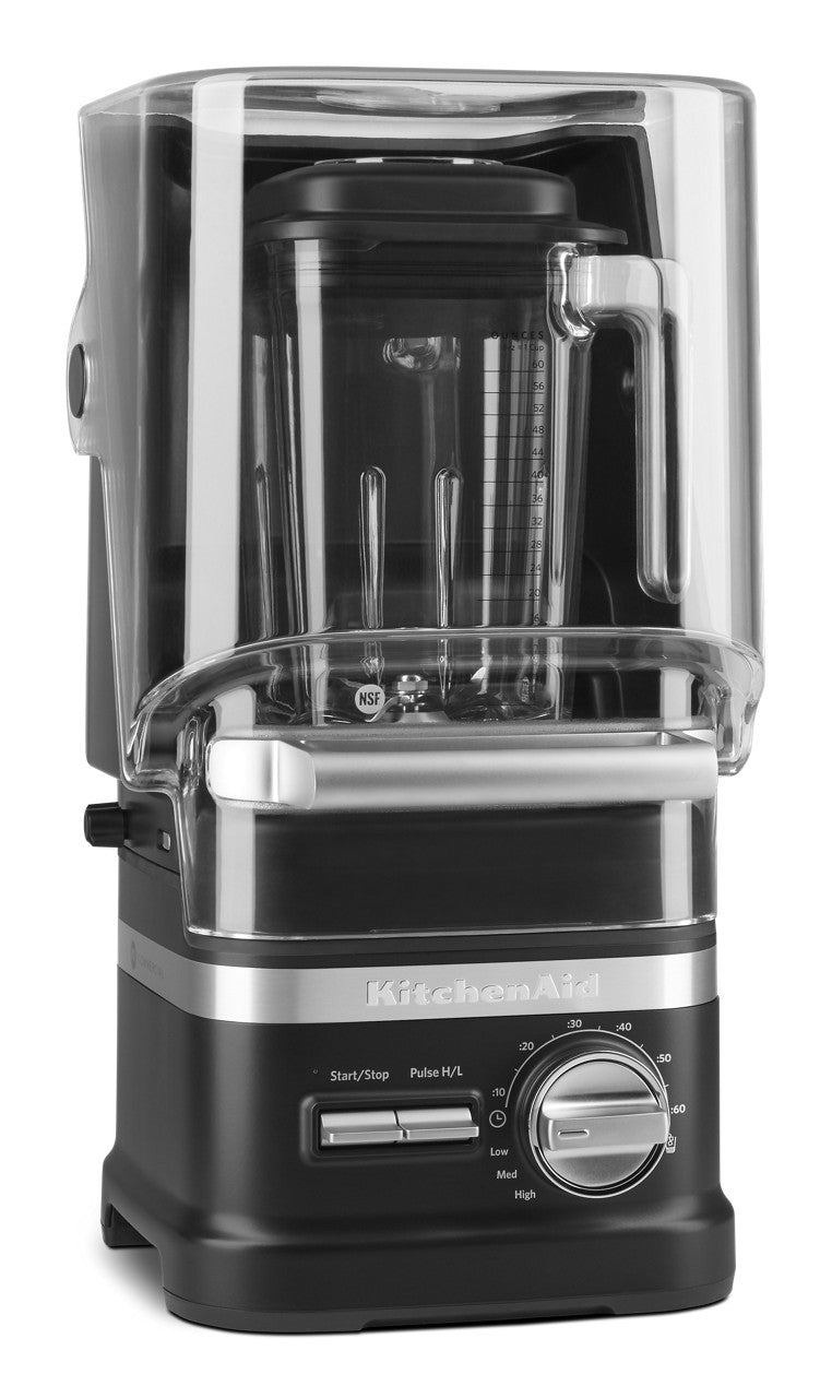 A black and silver KitchenAid Commercial Blender with a 60 oz blending jar features a clear noise-reducing enclosure. Its control panel includes start/stop, pulse/variable speed options, and a large dial marked from low to high.