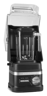 A black KitchenAid Commercial Blender with a 60 oz pitcher sits inside a clear sound enclosure. The blender features a metal control dial and buttons labeled Start/Stop and Pulse/Hi/Lo, with the KitchenAid logo beneath the controls.