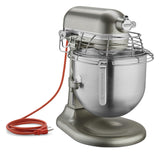 A metallic KitchenAid Commercial Stand Mixer with a robust, industrial design features an 8 quart bowl, safety guard, and a red power cord coiled beside it. The stainless steel bowl and KitchenAid branding stand out on its side.