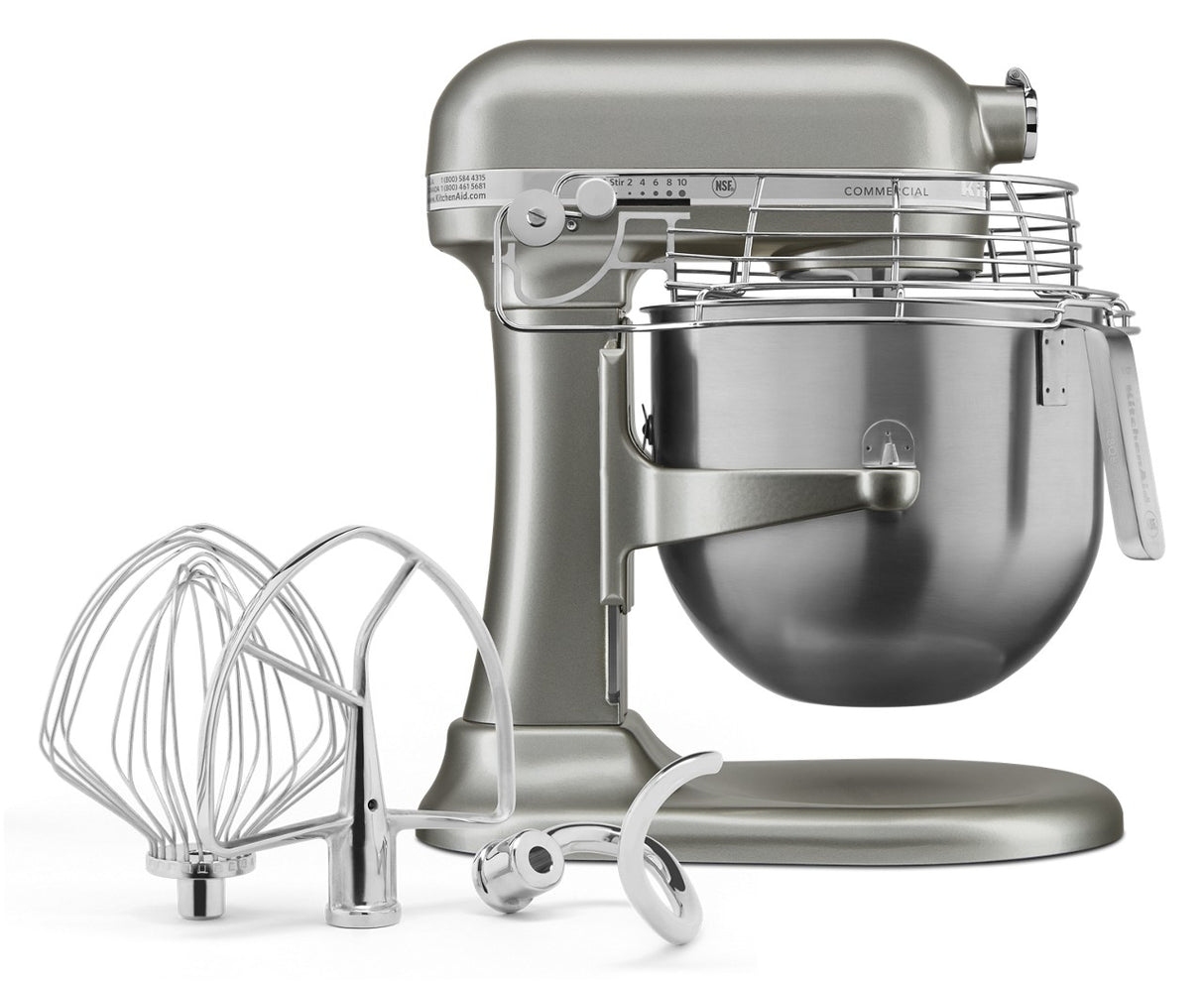 A silver KitchenAid Commercial Stand Mixer with an 8 quart bowl and safety guard is shown. In front, three metal attachments—a wire whisk, a flat beater, and a dough hook—rest on a white surface.