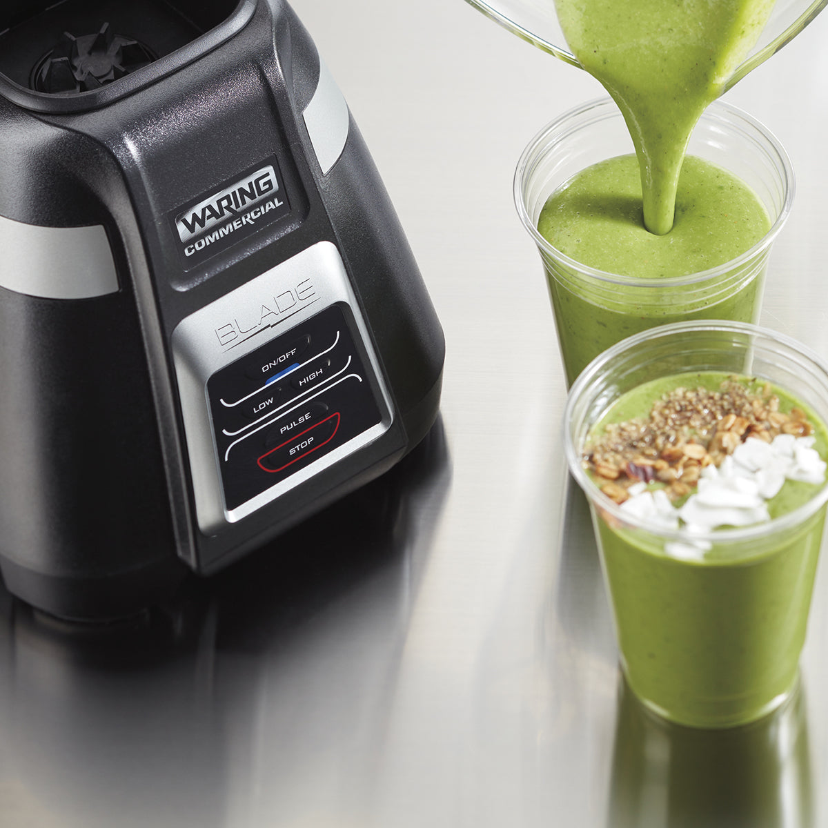 A close-up of a Waring Commercial Bar Blender with a 1.4 liter copolyester container beside two clear cups of green smoothie. One cup is being filled, while the other is topped with seeds, granola, and a drizzle of cream.
