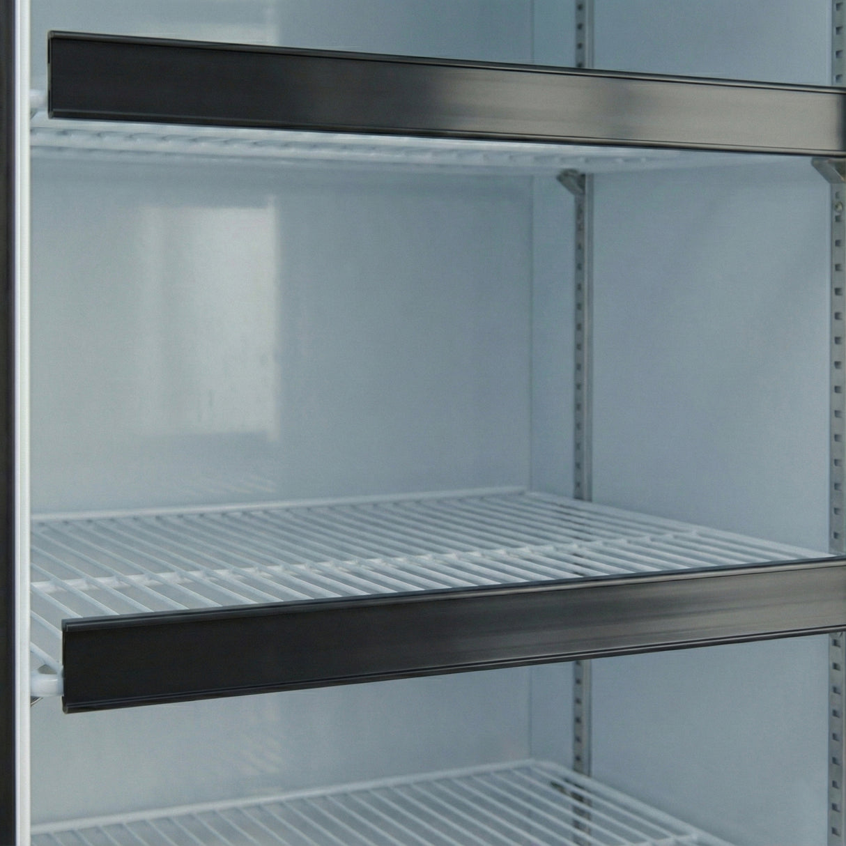 A close-up view of mostly empty wire shelves inside an EGM-36B commercial refrigerator. The white-coated metal shelves, often used with Empura Parts or a price tag set, highlight a sense of emptiness and limited stock in the clean interior.
