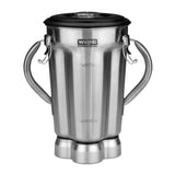 A Waring stainless steel blender container with two curved side handles, a black lid, and measurement markings on the front; the jar base has four grooved sections, giving it a shiny, industrial look.