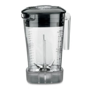 A clear copolyester MX Series Blender Container with a black lid and handle, vertical measurement markings in ounces and milliliters, and steel blades at the bottom. The jar sits on a gray rubber base and is empty, showing all interior details.