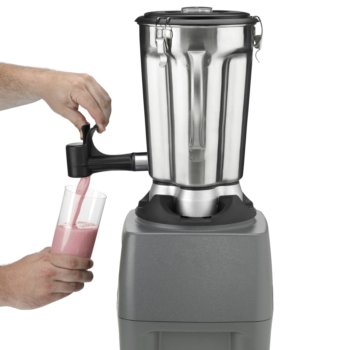 A person’s hands pour a pink smoothie from a spout attached to a heavy-duty Food Blender with a stainless steel container into a clear glass. The industrial-sized blender, on a gray base, is the focus as the smoothie streams smoothly.