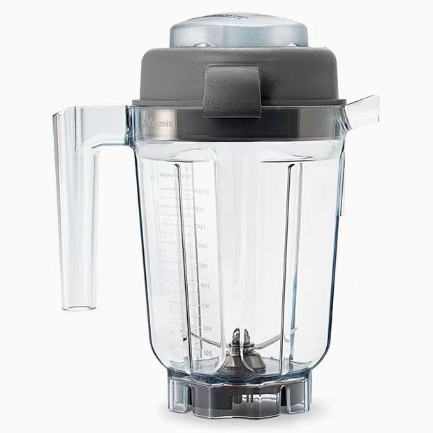 A clear, BPA free 32 oz blender container with measurement markings, a left-side handle, and a dark gray lid. Stainless steel blades sit at the base, designed to fit on a Vitamix blender. The background is plain white.