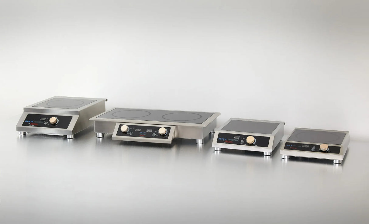 Four stainless steel countertop induction cooktops of various sizes are arranged in a row on a plain, reflective surface. Each features a digital display, control buttons, and a round knob. The background is light gray.