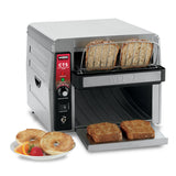 A stainless steel Waring CTS1000AL conveyor toaster with control dials toasts two slices of bread. Two toasted slices emerge on a tray. Beside it, a plate holds two bagel halves and mixed fruit, including a strawberry and melon slices.