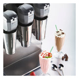 A triple spindle milkshake machine with three metal blending cups sits on the countertop. In front are two milkshakes—one pink with whipped cream and strawberries, one brown with whipped cream and chocolate shavings—plus spoons and chocolate pieces.