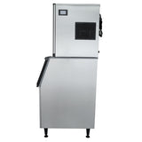 A commercial ice machine is shown from the side, featuring a rectangular upper unit with a black vent and control panel, mounted on a larger lower commercial ice storage bin with black trim and sitting on four short black legs.