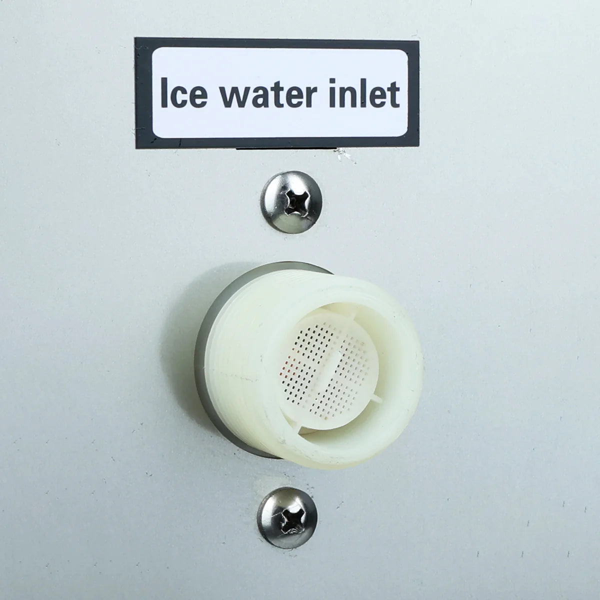 A close-up of a white plastic Ice water inlet on a light gray surface, commonly found on a commercial ice maker. The inlet features a mesh filter inside, with two metallic screws above and below it securing it in place.