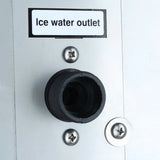 A close-up of a metal panel on a commercial ice maker shows a black circular outlet labeled Ice water outlet. Three screws secure the panel, and the label is printed in black text on a white background above the outlet.