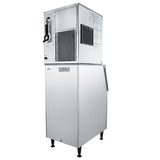 A large commercial ice maker with a silver metallic exterior stands on four black legs. The unit features vented panels, a coiled power cord, and a visible ColdSpace logo. Several instruction labels are displayed on the top section.