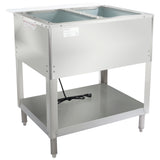 A stainless steel electric steam table with two open rectangular wells on top, a shelf below, four legs, and a visible power cord. The unit has a smooth surface and a “Caution: Hot Surface” label on the front left corner.