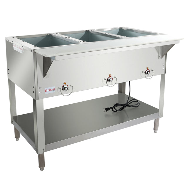 A commercial stainless steel 3-well steam table features control knobs on the front, an open lower shelf, four sturdy legs, and a power cord resting on the shelf. The top includes three rectangular wells for holding food pans.