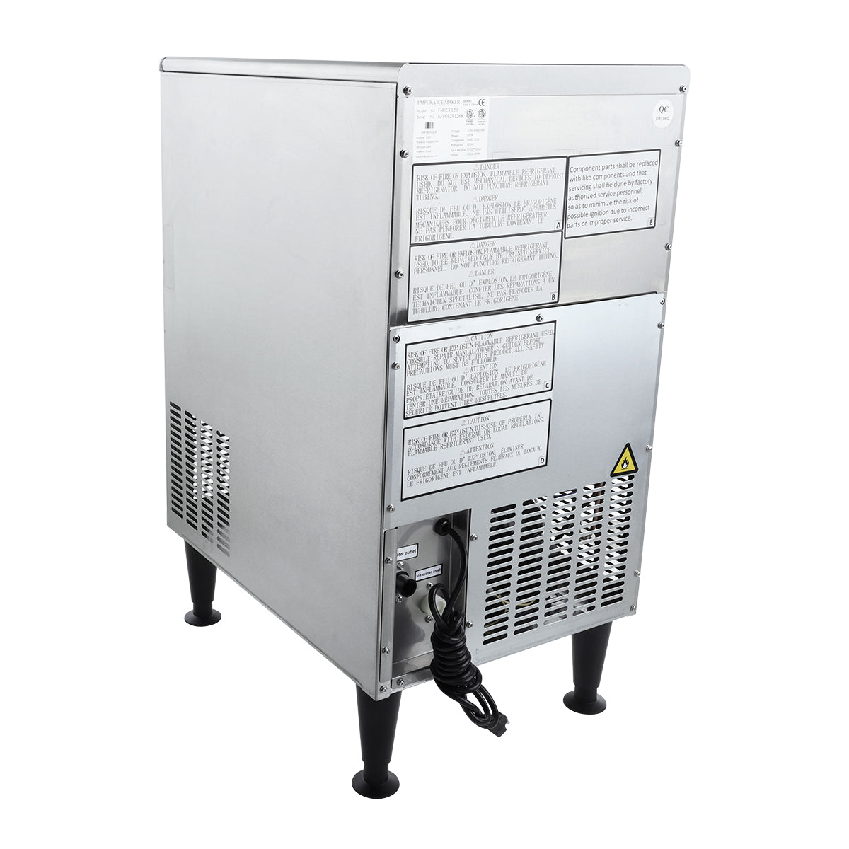 A commercial ice machine with a rectangular, industrial design stands on four black legs. The back panel features warning labels, ventilation grilles, a yellow caution symbol, and a black power cord. This stainless steel ice maker is built for durability and performance.
