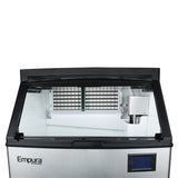 A commercial ice machine with an open lid reveals its clean, white interior and metal ice grid. The front panel displays the Empura ICE MACHINES logo in black and has a blue digital screen on the right side, highlighting this efficient undercounter ice maker.