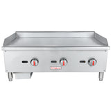 A stainless steel commercial gas griddle with three red-handled control knobs, a grease tray on the left, raised sides, and an Empura brand label. This countertop griddle features four short legs and a flat cooking surface.