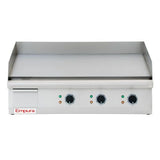 A stainless steel Empura countertop electric griddle with three control knobs and indicator lights on the front panel, a flat cooking surface, and raised sides and back for splatter protection. The Empura brand is visible on the lower left corner.