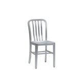 A silver metal Anna Side Chair with a minimalist design, featuring a slightly curved backrest with vertical slats and a flat rectangular seat. Crafted from brushed aluminum, this indoor outdoor chair has a sleek, industrial look against a plain white background.