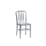 A silver metal Anna Side Chair with a minimalist design, featuring a slightly curved backrest with vertical slats and a flat rectangular seat. Crafted from brushed aluminum, this indoor outdoor chair has a sleek, industrial look against a plain white background.