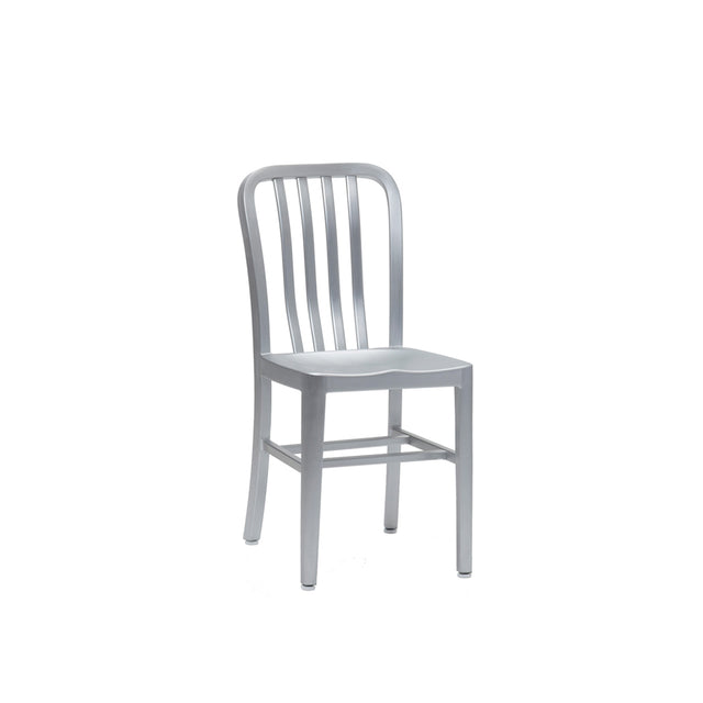 A silver metal Anna Side Chair with a minimalist design, featuring a slightly curved backrest with vertical slats and a flat rectangular seat. Crafted from brushed aluminum, this indoor outdoor chair has a sleek, industrial look against a plain white background.