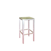 The Anna Barstool is a tall, square, backless stool with an aluminum seat and four straight legs. Its pale pink finish and minimalist design suit both outdoor/indoor spaces. The supportive bars near the base add stability. Background is plain white.