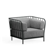 A modern Cannolè Lounge Armchair with a black steel wire back and metal frame featuring vertical, curved lines, plus thick gray cushions. Its airy, open structure and four straight legs make it ideal as an outdoor armchair against a white background.