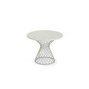 A round, white Como Side Table with a solid top and an open, geometric steel wire base that flares outward in a lattice shape. This modern, minimalist indoor/outdoor side table is centered on a plain white background.
