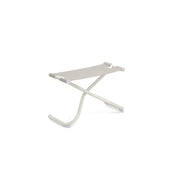 A minimalist, modern stool with a white metal frame and light beige striped EMU-Tex fabric seat. Inspired by the Snooze Ottoman, its X-shaped curved legs have rubber caps, and the seat is stretched taut. Perfect as an outdoor ottoman. Plain white background.