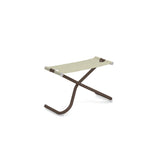 A minimalist, modern Snooze Ottoman with a brown X-shaped metal frame and a beige EMU-Tex fabric seat. The legs curve outward at the base, finished with white caps for stability. This outdoor ottoman is photographed on a white background.