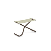 A minimalist, modern Snooze Ottoman with a brown X-shaped metal frame and a beige EMU-Tex fabric seat. The legs curve outward at the base, finished with white caps for stability. This outdoor ottoman is photographed on a white background.