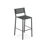 The Segno Stacking Barstool is a modern black steel barstool with a slatted seat and backrest, four straight legs, and a footrest. Its sleek, minimalist design makes it ideal as an outdoor barstool, set against a plain white background.