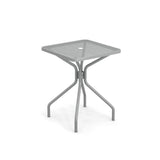 The Cambi Table is a modern, square outdoor indoor table featuring a mesh top with a central hole. Supported by four curved legs that connect in the middle, its gray finish highlights a minimalist, industrial design.